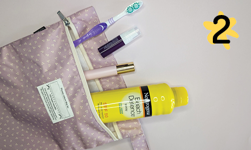 A pink wet bag with a subtle patterned design, repurposed as a toiletry bag. The bag is unzipped to reveal a toothbrush, a small spray bottle, a mascara tube, and a bottle of Neutrogena sunscreen lotion with SPF 50.